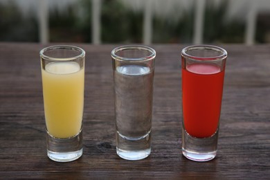 Photo of Shots with lime juice, tequila and sangria as colors of mexican flag on wooden table. Traditional serving