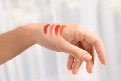 Photo of Woman testing and choosing lip gloss color on hand, closeup