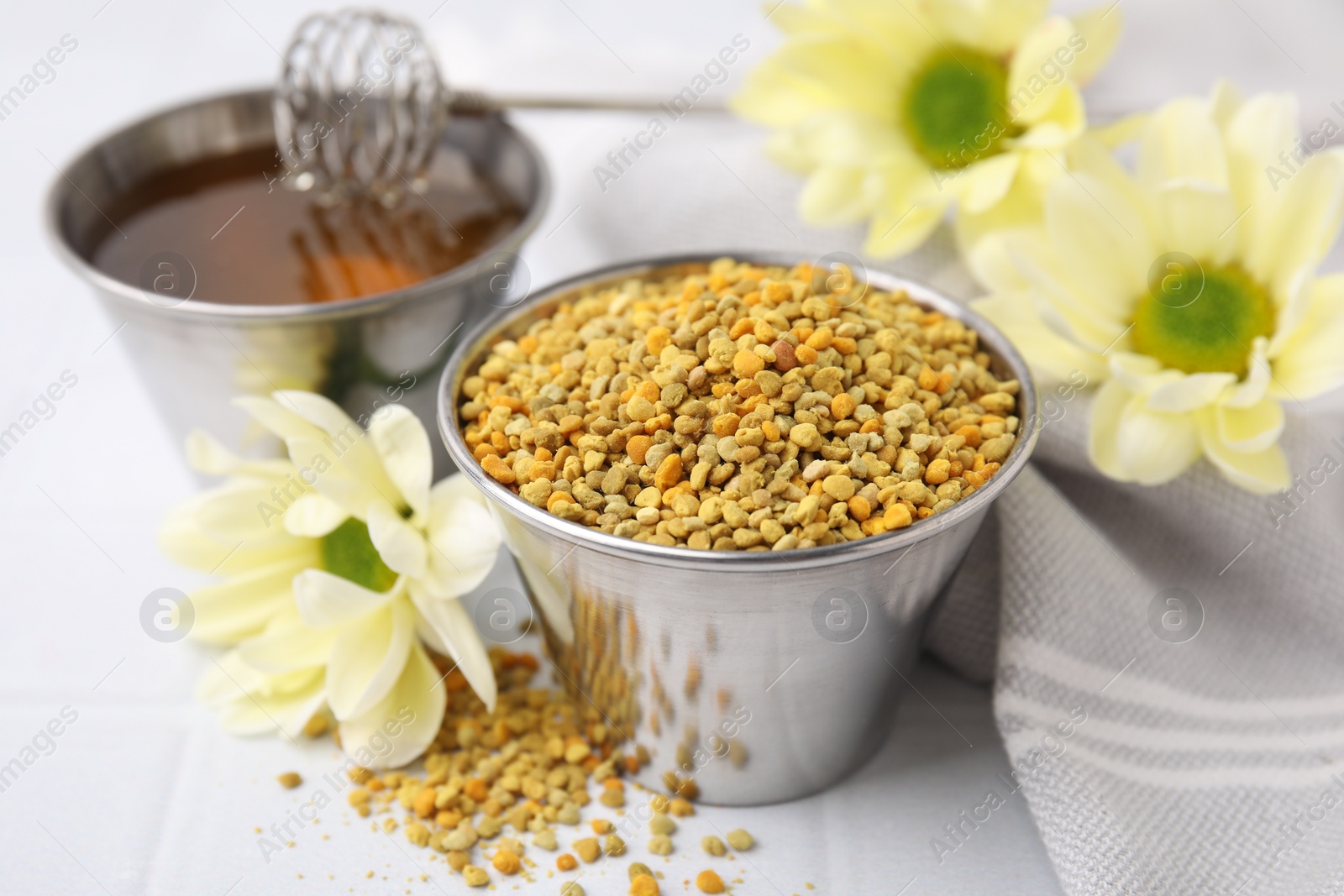 Photo of Fresh bee pollen granules and flowers on white table, closeup