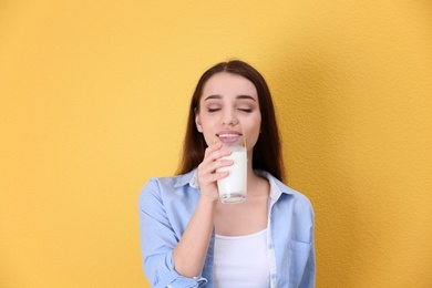 Beautiful young woman drinking milk on color background