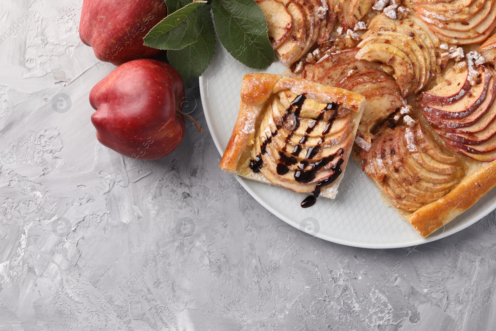 Photo of Tasty apple pie with chocolate topping, fresh fruits and green leaves on light grey textured table, flat lay. Space for text