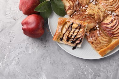 Photo of Tasty apple pie with chocolate topping, fresh fruits and green leaves on light grey textured table, flat lay. Space for text