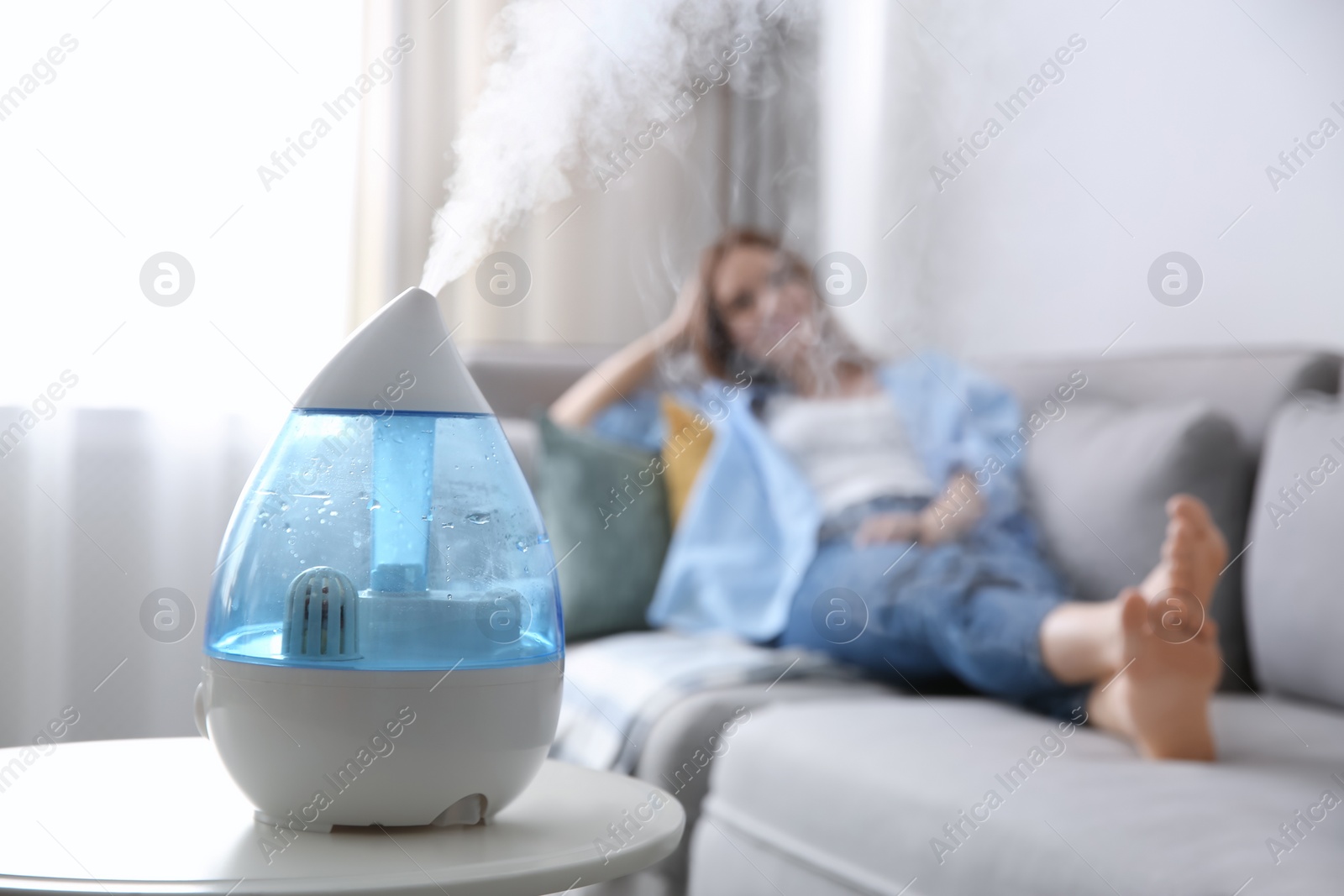 Photo of Modern air humidifier and blurred woman resting on background