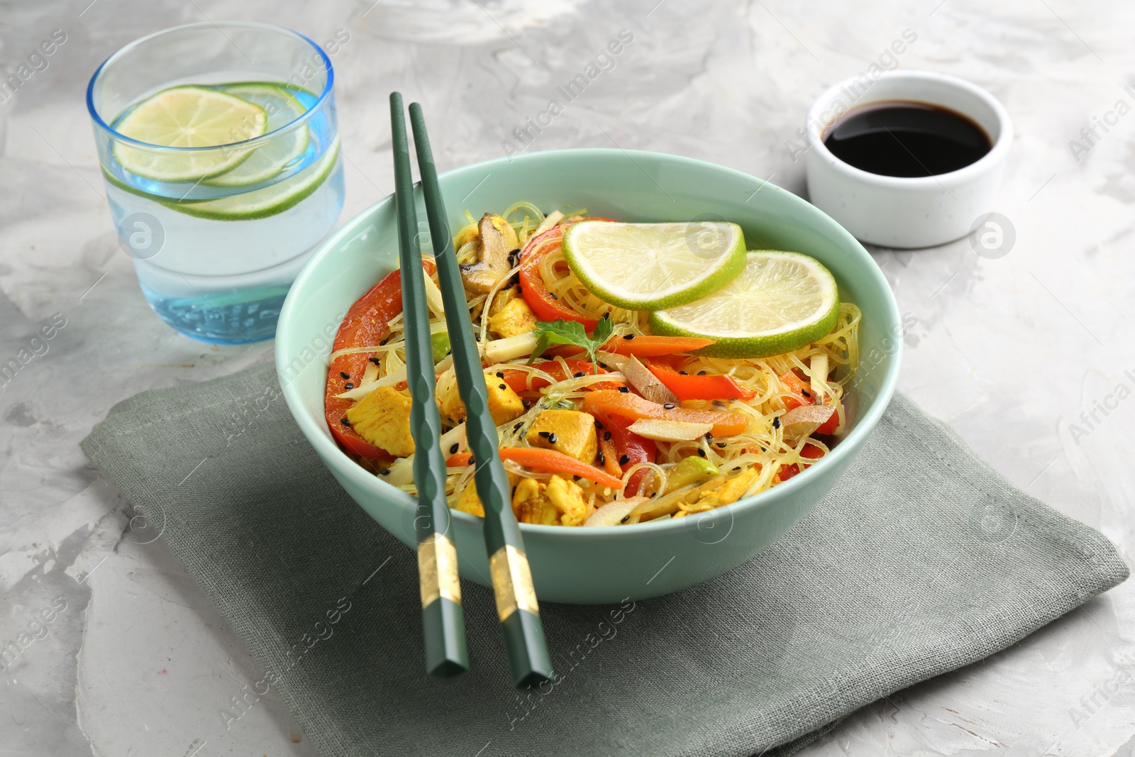 Photo of Stir-fry. Delicious cooked noodles with chicken and vegetables in bowl served on gray textured table