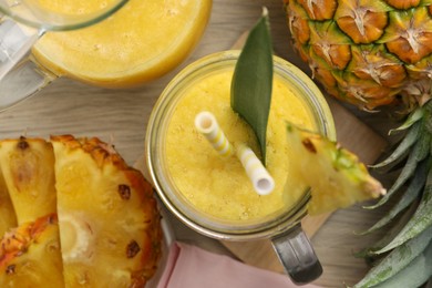 Tasty pineapple smoothie and fruit on wooden table, flat lay