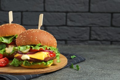Photo of Delicious burgers with beef patty and tomatoes on grey table. Space for text