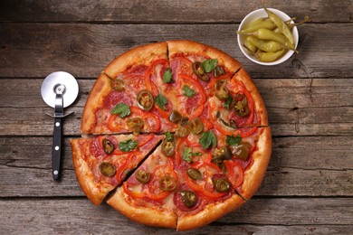 Photo of Delicious pizza Diablo, pickled peppers and cutter on wooden table, flat lay