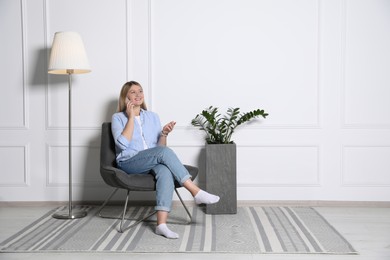 Young woman talking on phone in armchair at home, space for text. Interior design