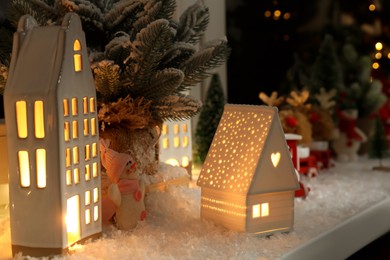 Photo of Christmas atmosphere. Beautiful glowing houses, fir trees, artificial snow and toys on window sill indoors, closeup