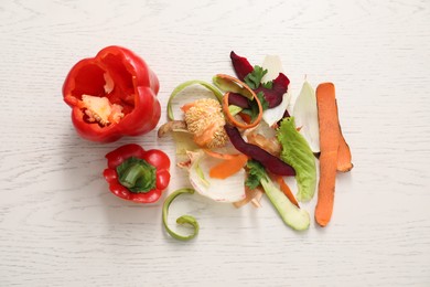 Peels of fresh vegetables and cut pepper on white wooden table, flat lay