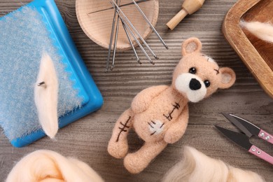 Photo of Felted bear, wool and different tools on wooden table, flat lay