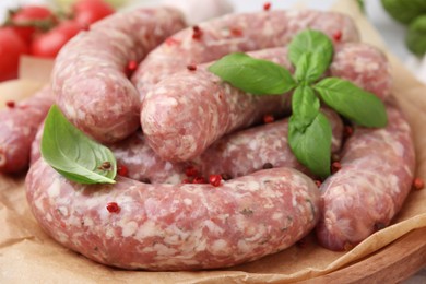 Photo of Raw homemade sausages, basil leaves and peppercorns on wooden board, closeup