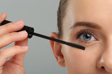 Photo of Woman applying mascara on grey background, closeup