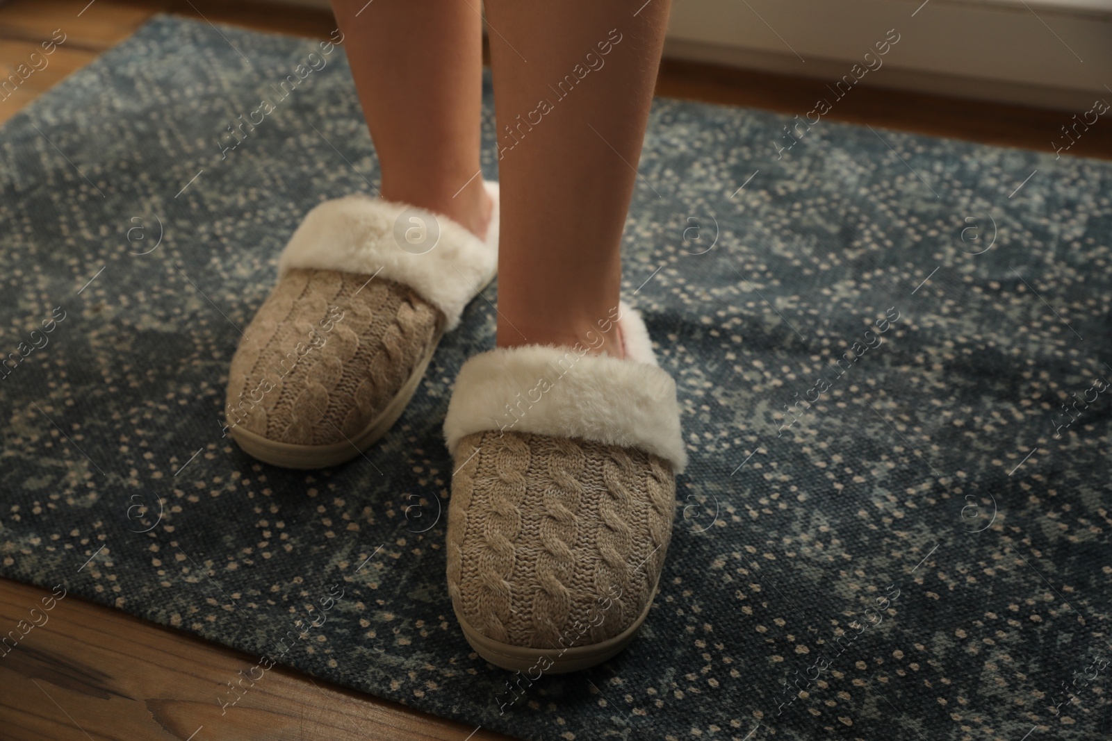 Photo of Woman wearing warm beige slippers on rug, closeup