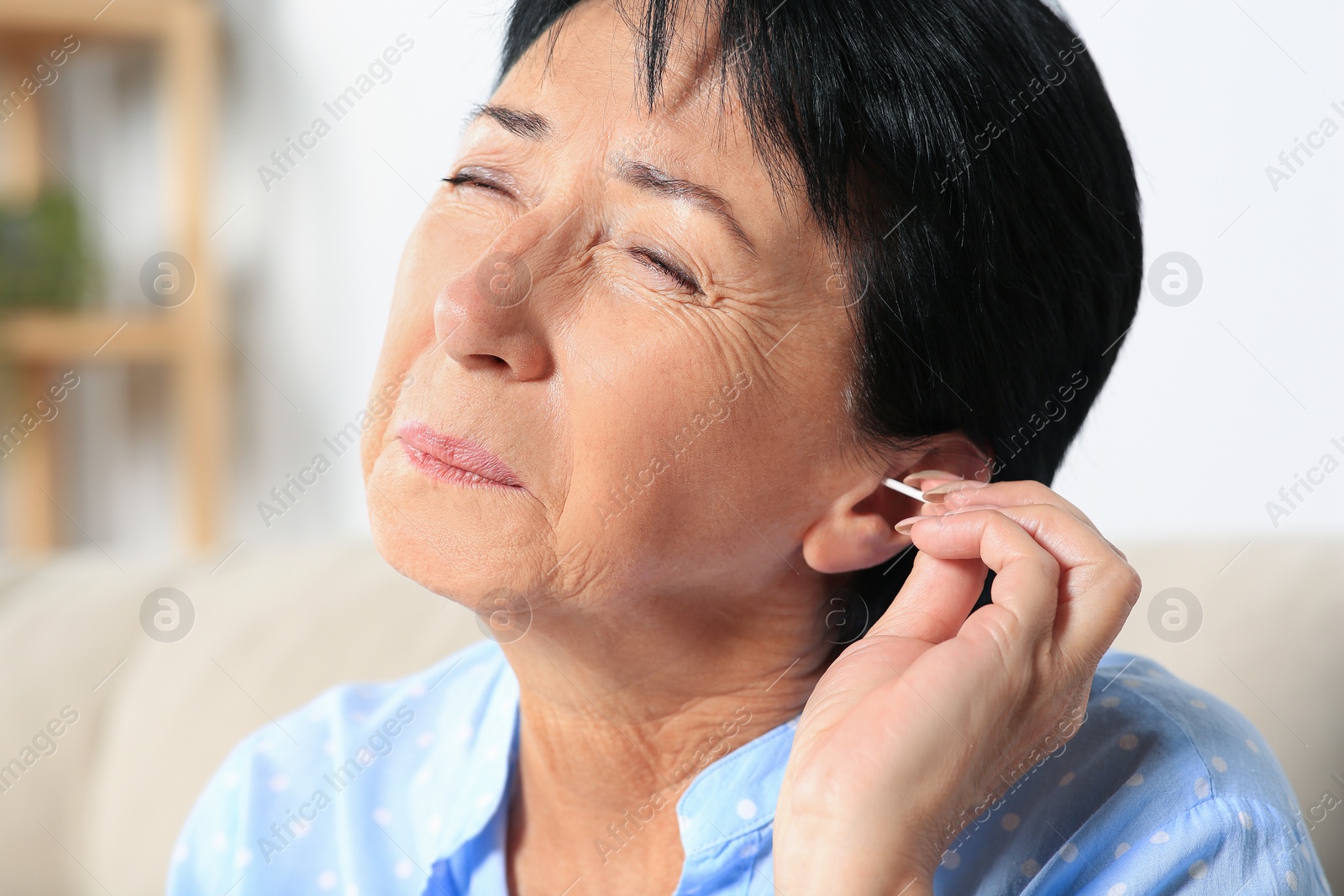 Photo of Senior woman cleaning ear with cotton swab at home, closeup