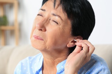 Photo of Senior woman cleaning ear with cotton swab at home, closeup