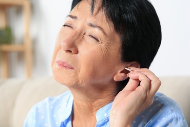 Senior woman cleaning ear with cotton swab at home, closeup