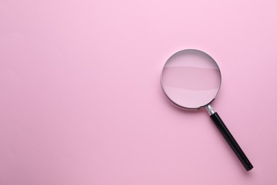 Magnifying glass on pink background, top view. Space for text