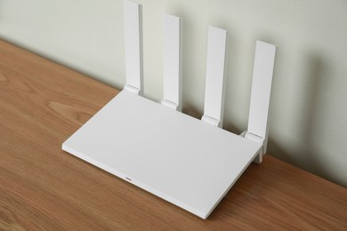 New modern Wi-Fi router on wooden table near white wall