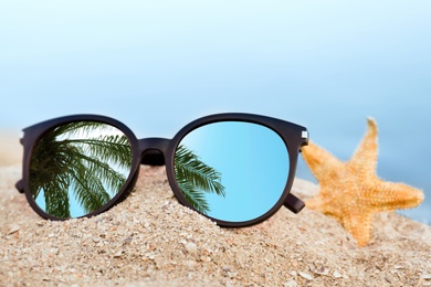 Image of Green palm leaves mirroring in sunglasses on sandy beach with starfish