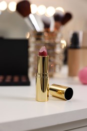 Photo of Red lipstick and other cosmetic products on white table in makeup room, selective focus