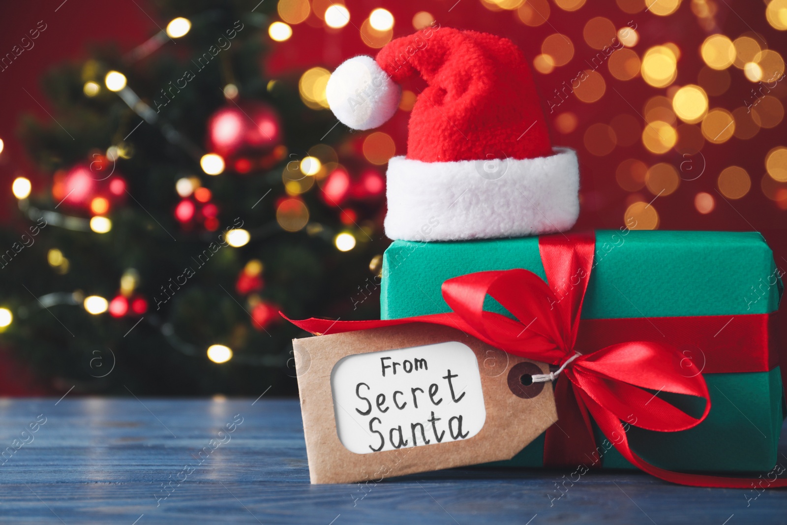 Photo of Present from secret Santa on blue wooden table against blurred Christmas tree, space for text