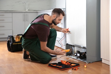 Photo of Male technician in uniform repairing refrigerator indoors