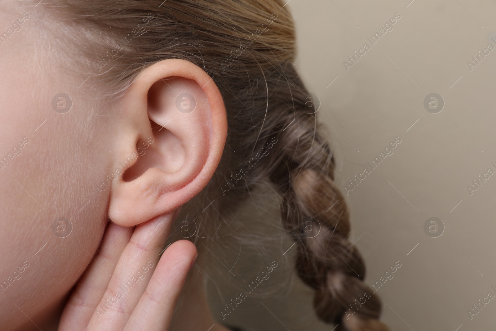 Photo of Cute little girl showing hand to ear gesture on beige background, closeup