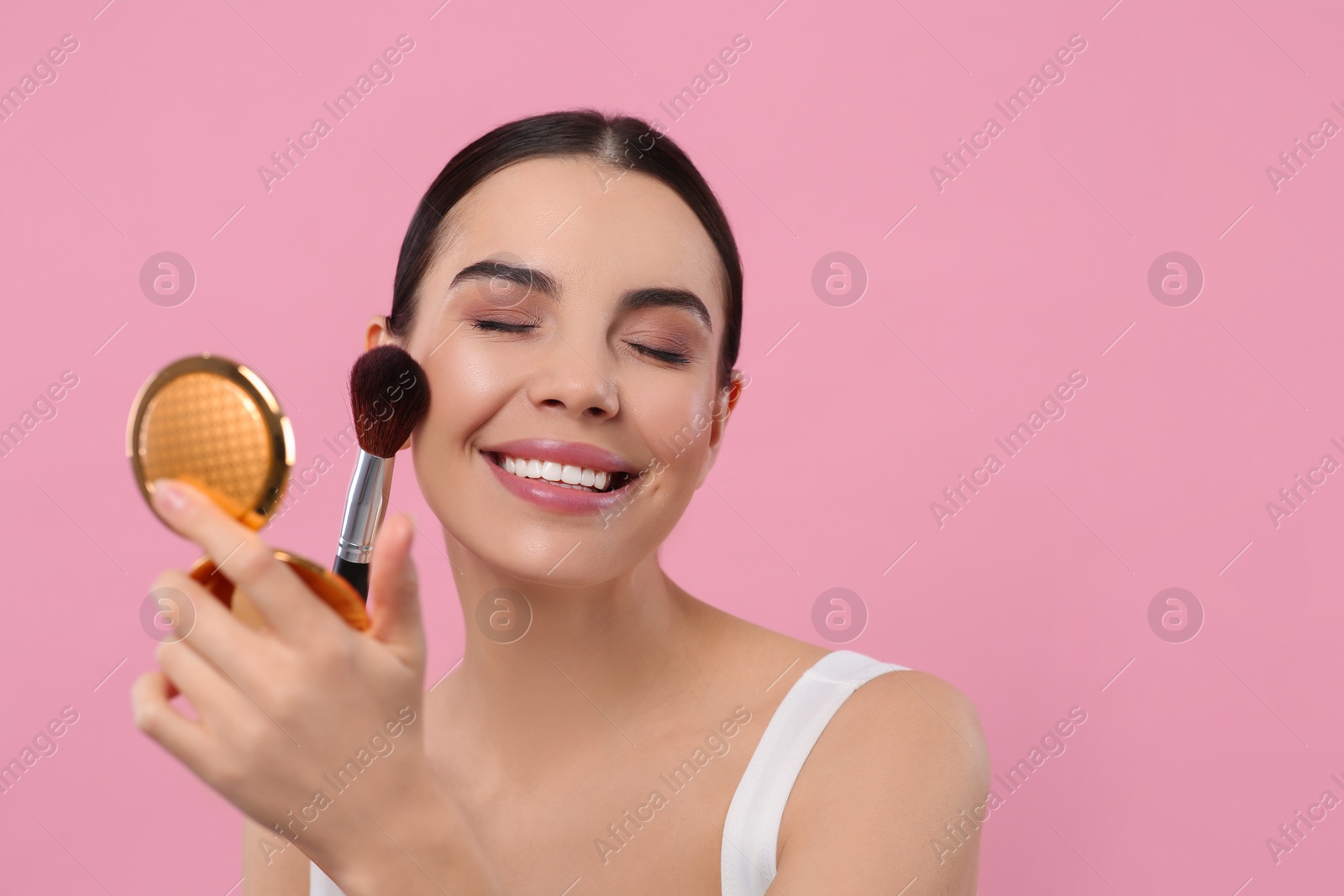 Photo of Beautiful woman with cosmetic pocket mirror applying makeup on pink background, space for text