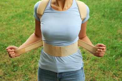 Closeup view of woman with orthopedic corset on green grass outdoors