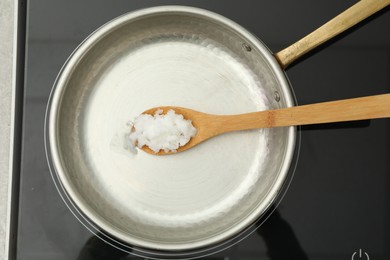 Photo of Frying pan with coconut oil and wooden spatula on induction stove, top view. Healthy cooking