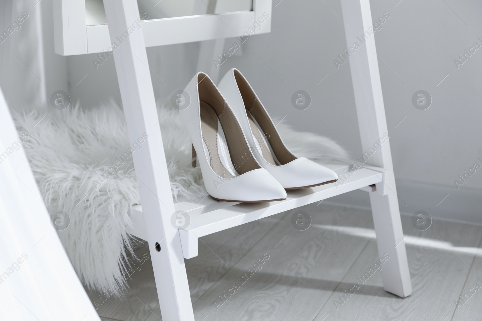 Photo of Pair of white wedding high heel shoes on wooden rack indoors