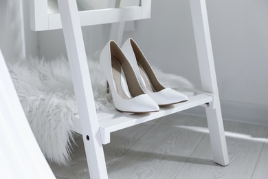Photo of Pair of white wedding high heel shoes on wooden rack indoors