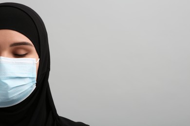 Muslim woman in hijab and medical mask on light gray background, space for text