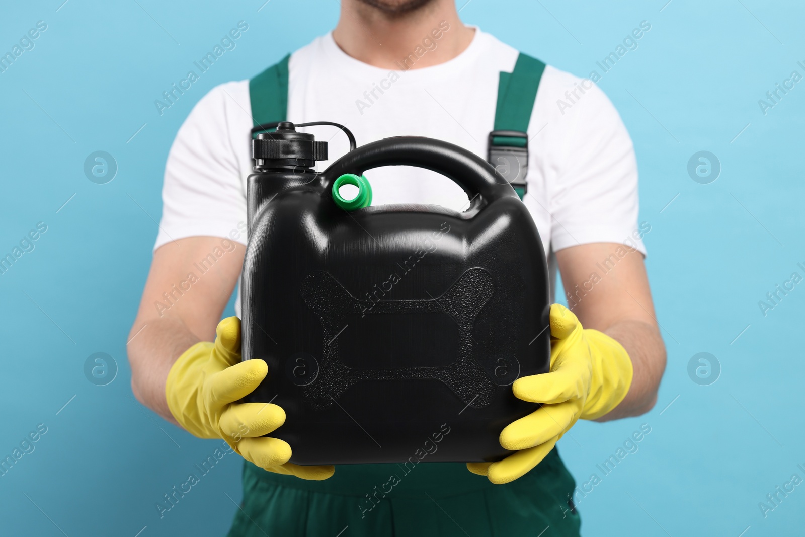 Photo of Man in rubber gloves holding black canister on light blue background, closeup