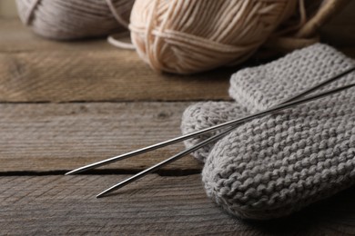 Photo of Soft colorful yarns, knitted socks and metal needles on wooden table, closeup