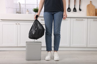 Photo of Woman taking garbage bag out of trash bin in kitchen, closeup