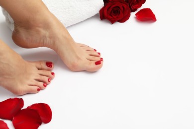 Photo of Woman with stylish red toenails after pedicure procedure and rose petals on white background, closeup. Space for text