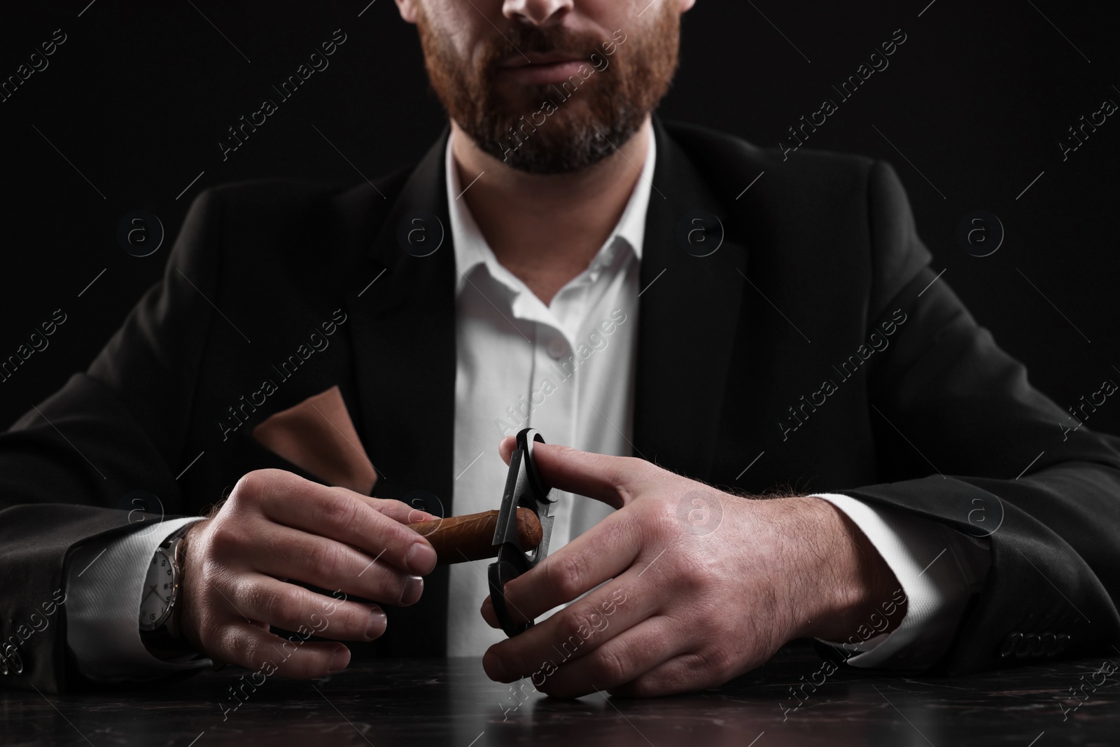 Photo of Man cutting tip of cigar at dark marble table, closeup