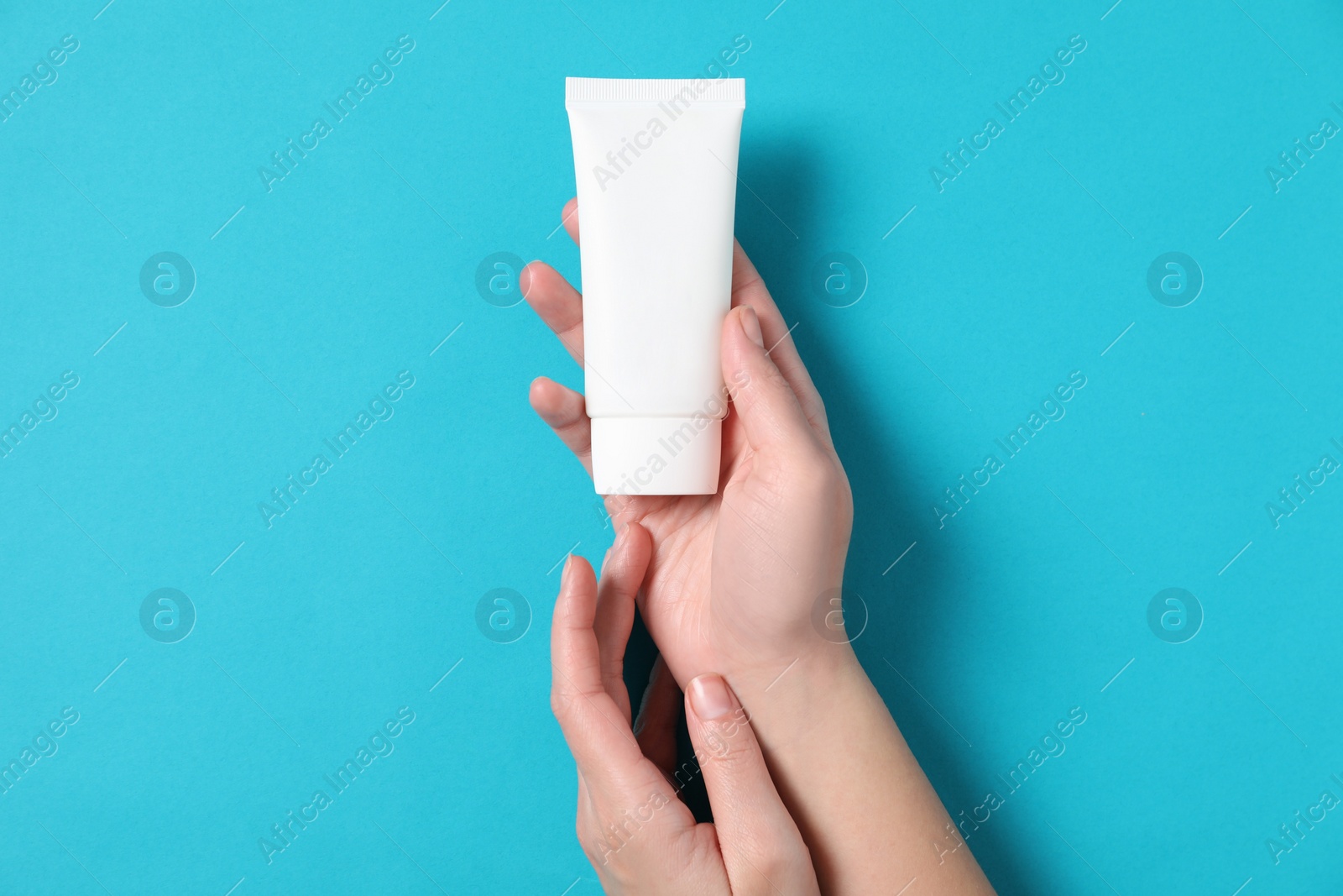 Photo of Woman with tube of hand cream on light blue background, top view