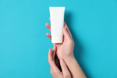 Woman with tube of hand cream on light blue background, top view