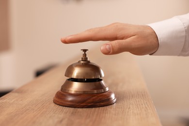 Man ringing service bell at wooden reception desk in hotel, closeup