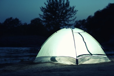 Photo of Small camping tent glowing in twilight outdoors. Space for text