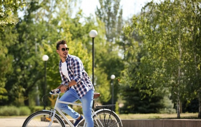 Handsome young hipster man riding bicycle in park