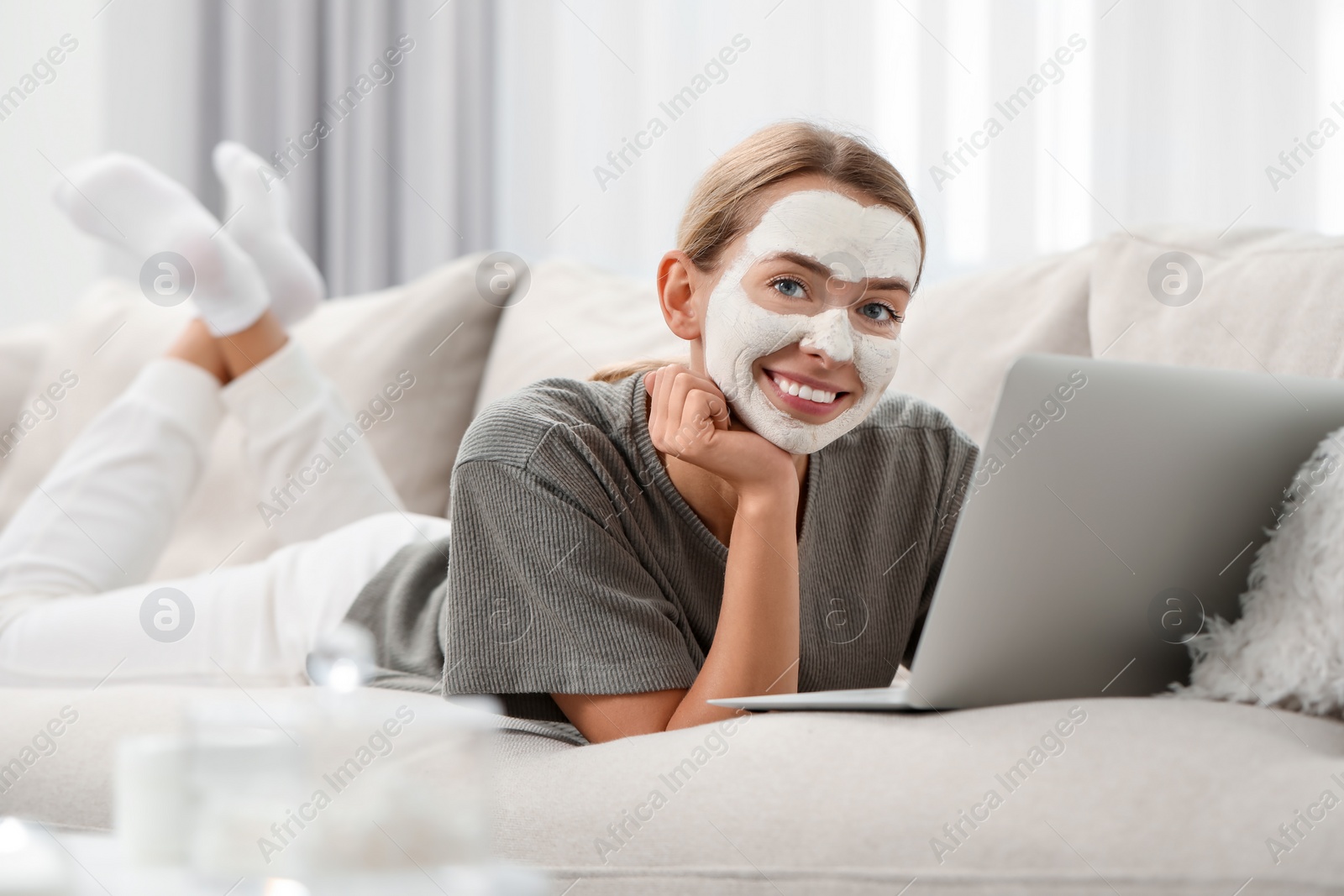 Photo of Young woman with face mask using laptop on sofa at home. Spa treatments