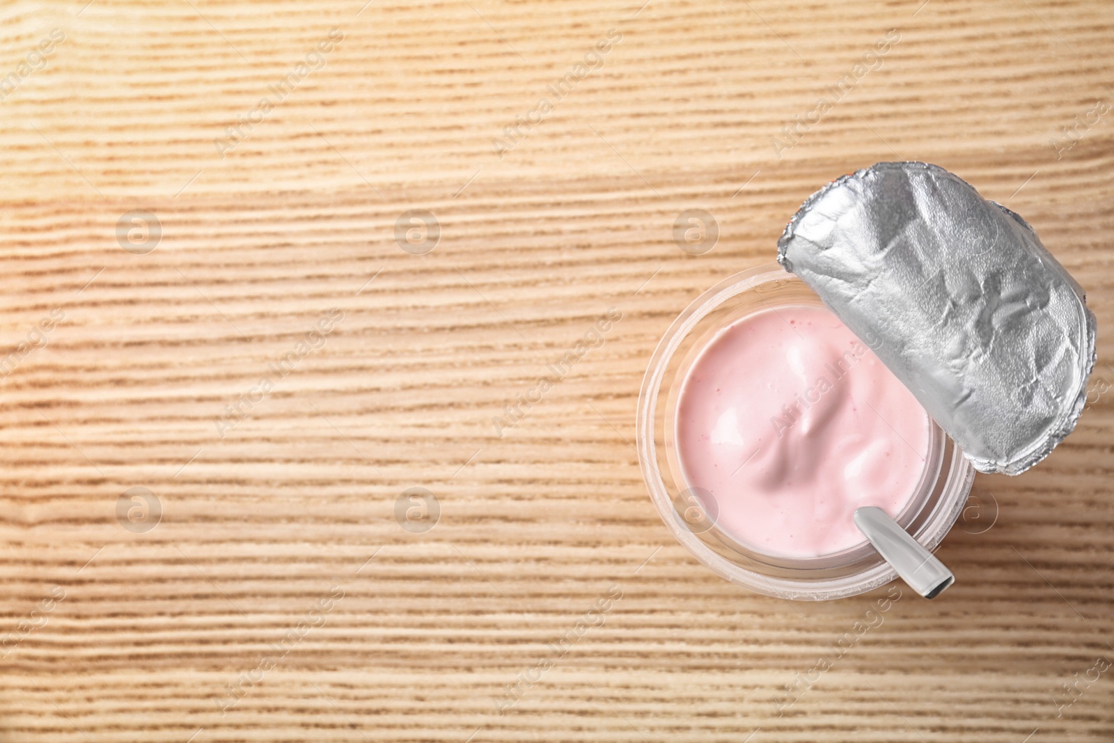 Photo of Plastic cup with tasty yogurt on wooden background, top view