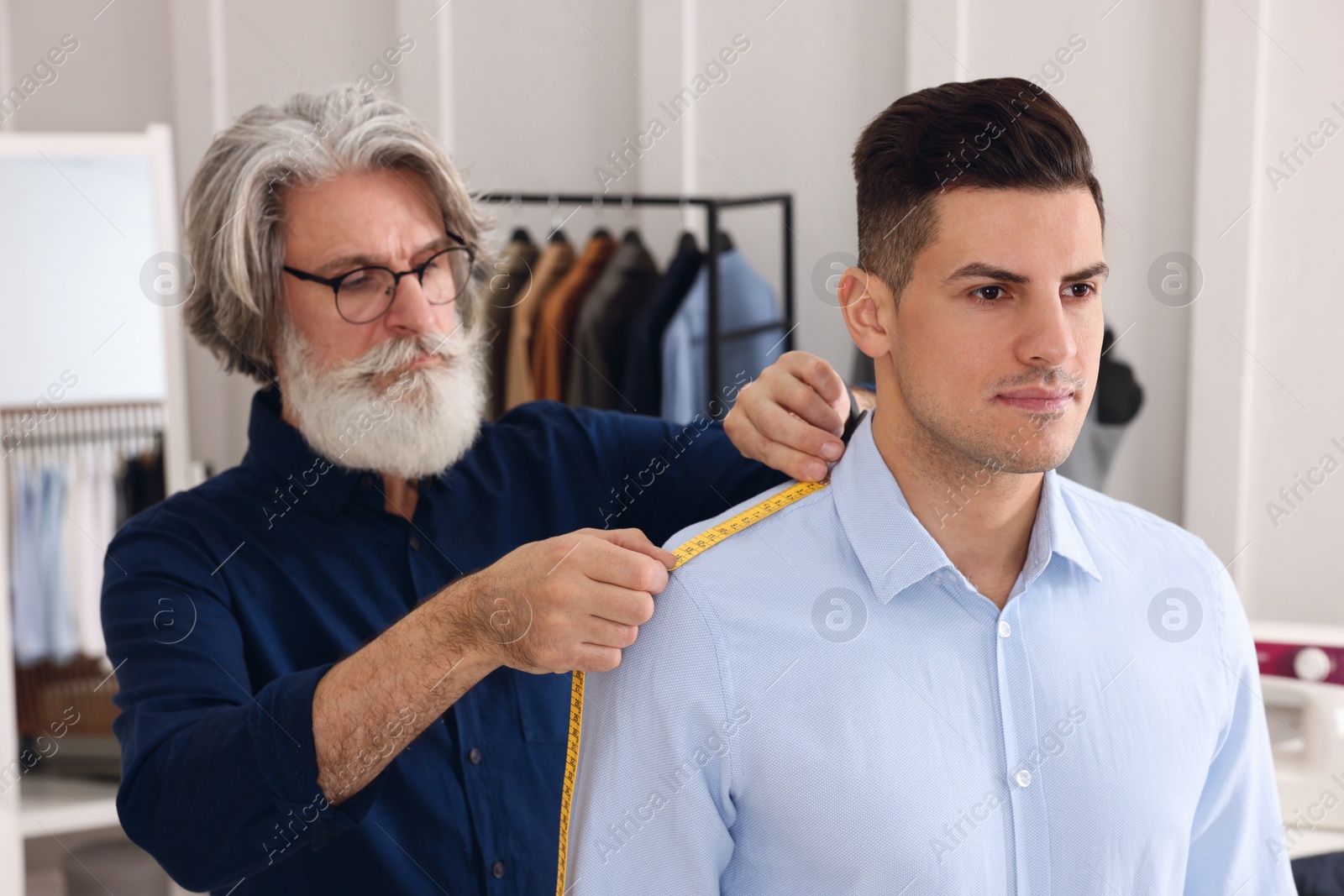 Photo of Professional tailor measuring shoulder seam length on client's shirt in atelier