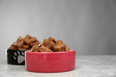 Wet pet food in feeding bowls on light grey table, space for text