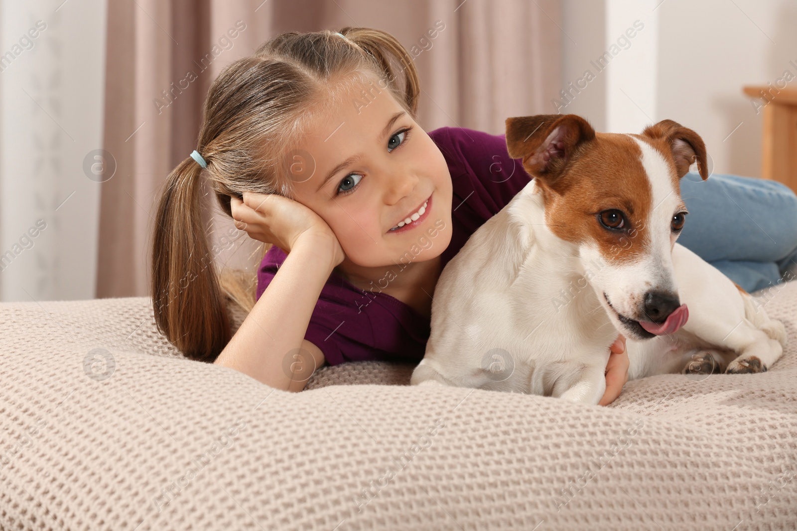 Photo of Cute girl with her dog on bed indoors. Adorable pet