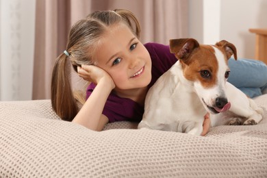 Photo of Cute girl with her dog on bed indoors. Adorable pet